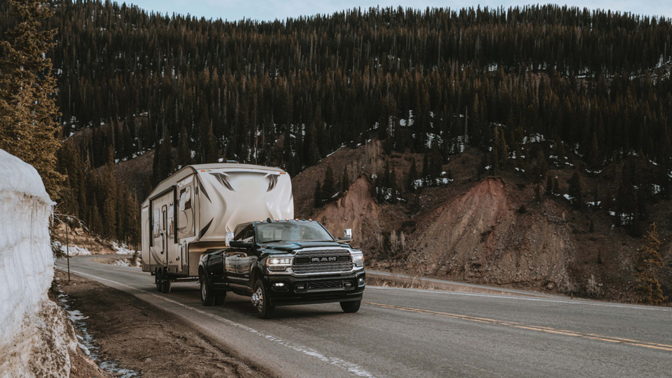 A Ram 3500 pulls a large camper up a steep, mountainous road.